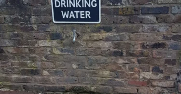 An outdoor drinking water tap with a sign on a stone wall in England